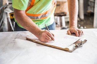 Mann schreibt auf Papier in einem Klemmbrett